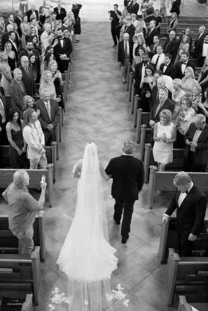 black+white photo of bride with father, walking down aisle during church wedding