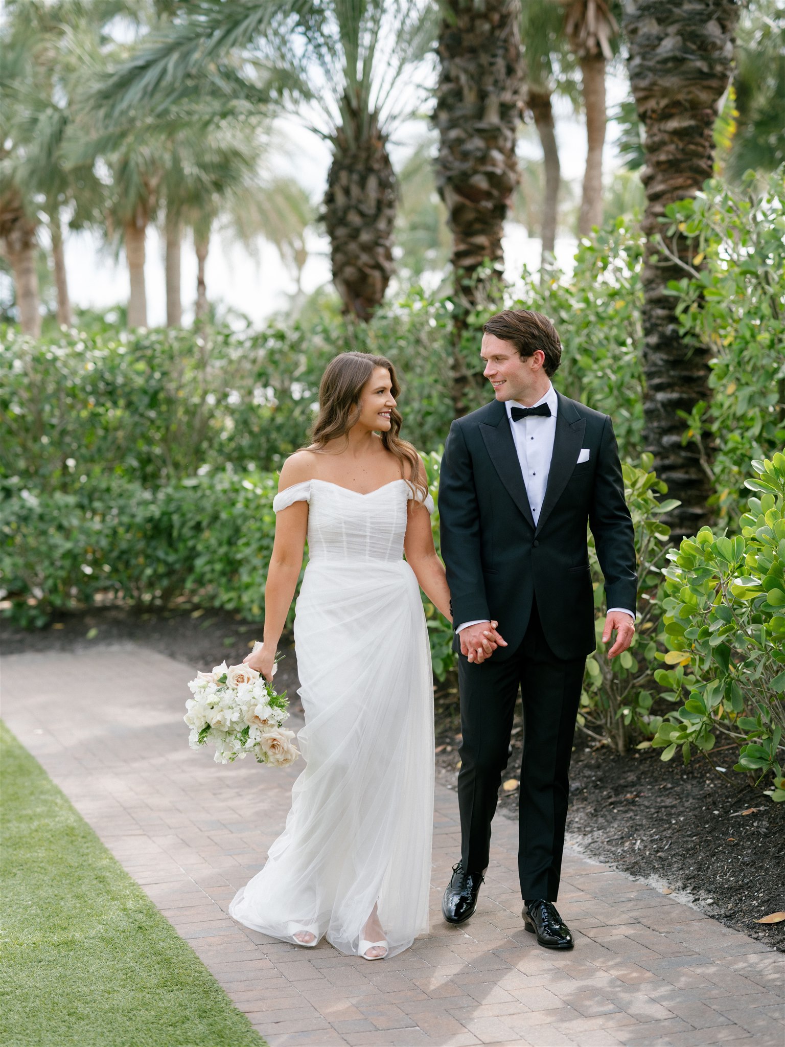 A bride and groom walk to the reception after their ceremony in Florida under the palm trees.