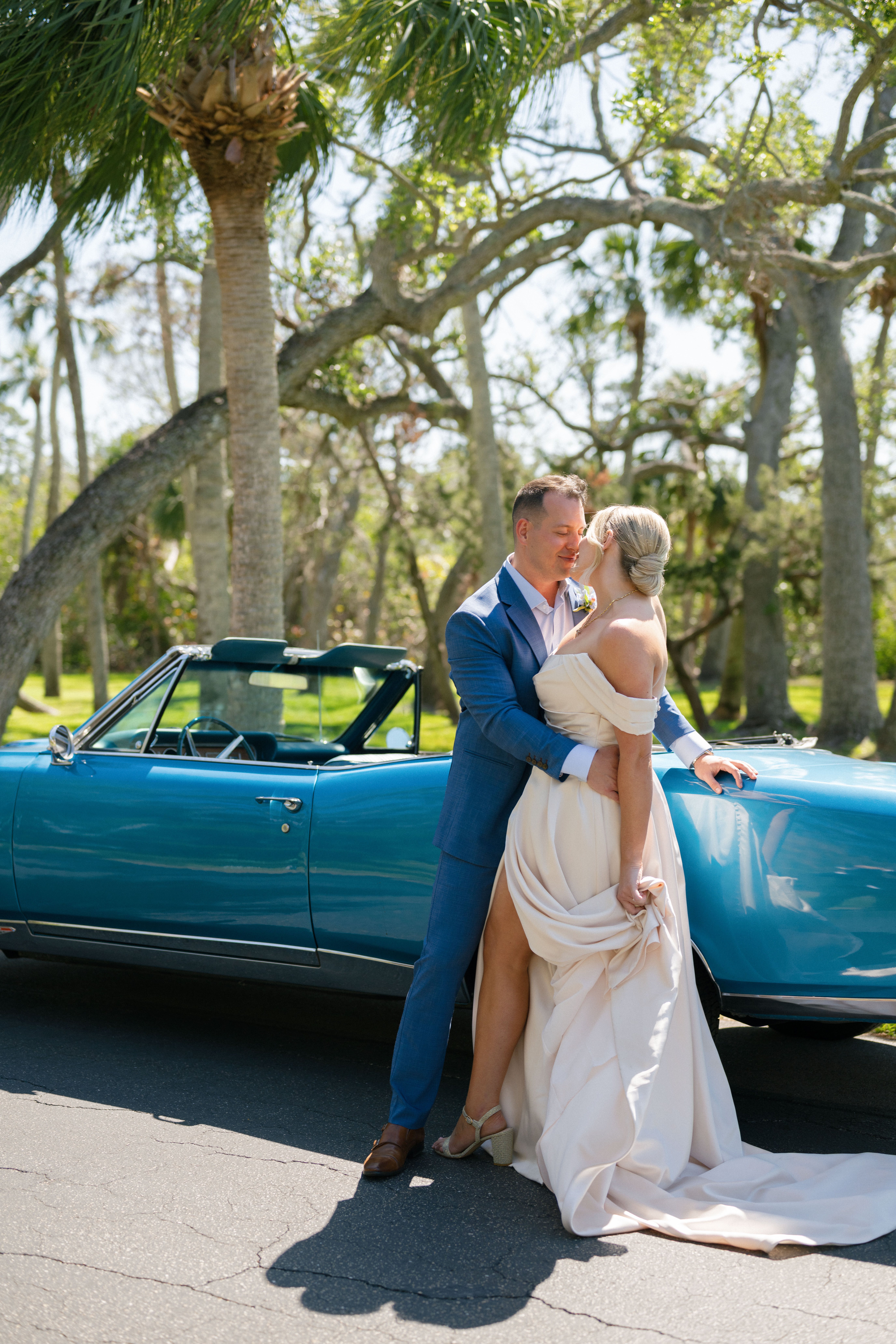 Bride and groom posing in front of a blue classic car in Naples, FL.