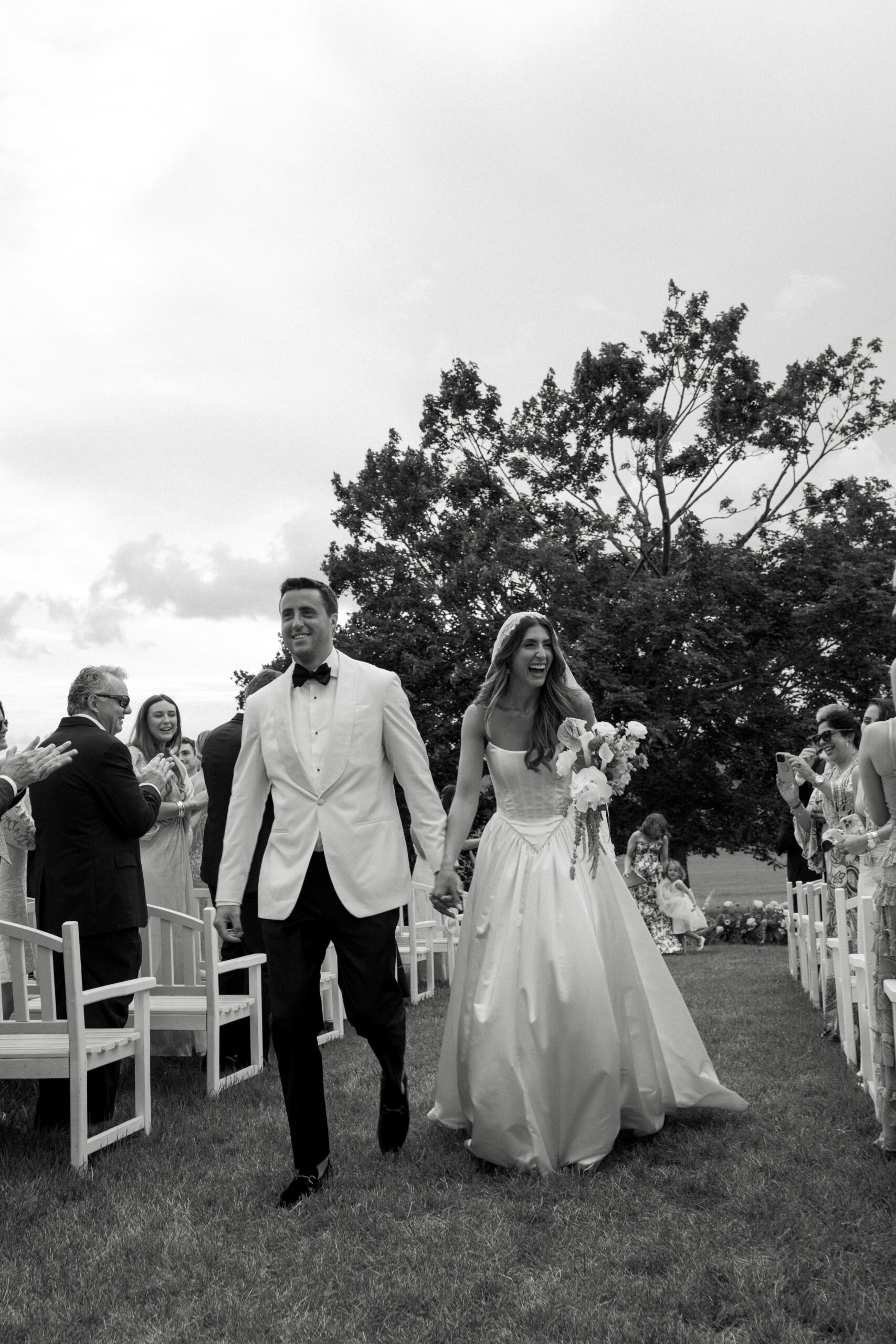 A black and white photo of a bride and groom smiling as they walk back down the aisle after saying 'I do'.