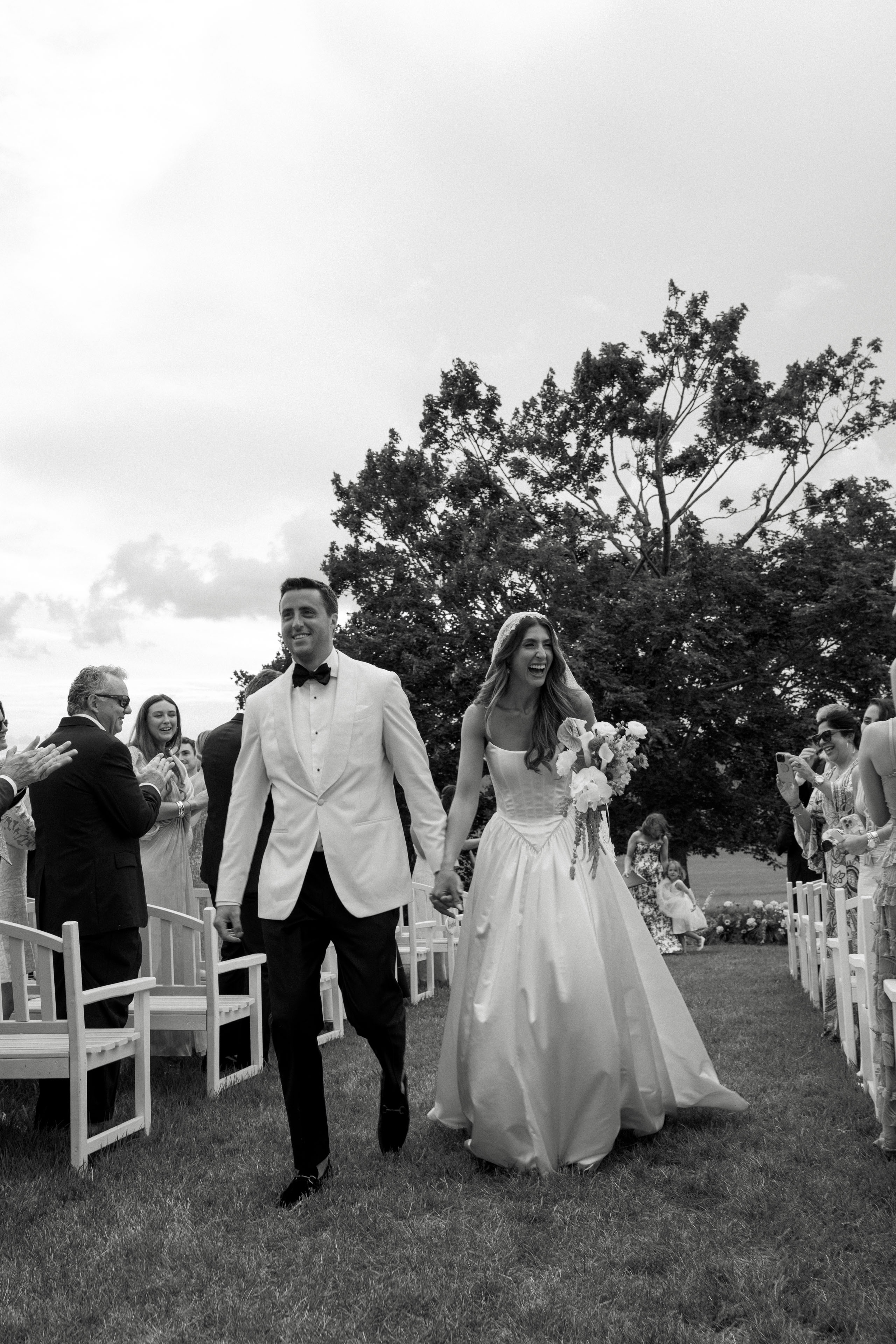 A black and white photo of a bride and groom smiling as they walk back down the aisle after saying 'I do'.