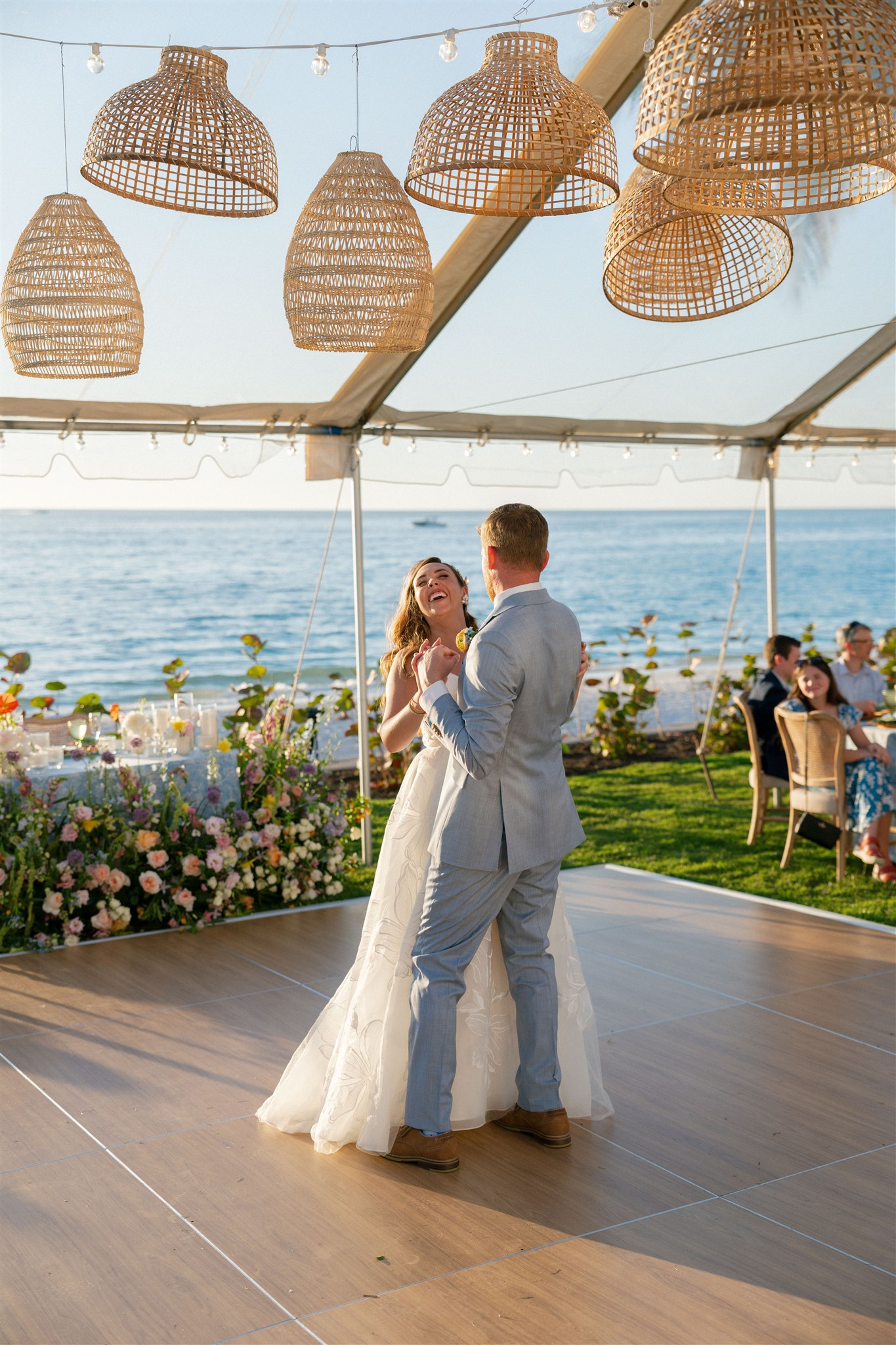 A bride and groom sharing their first dance overlooking the ocean in a tented wedding reception space.