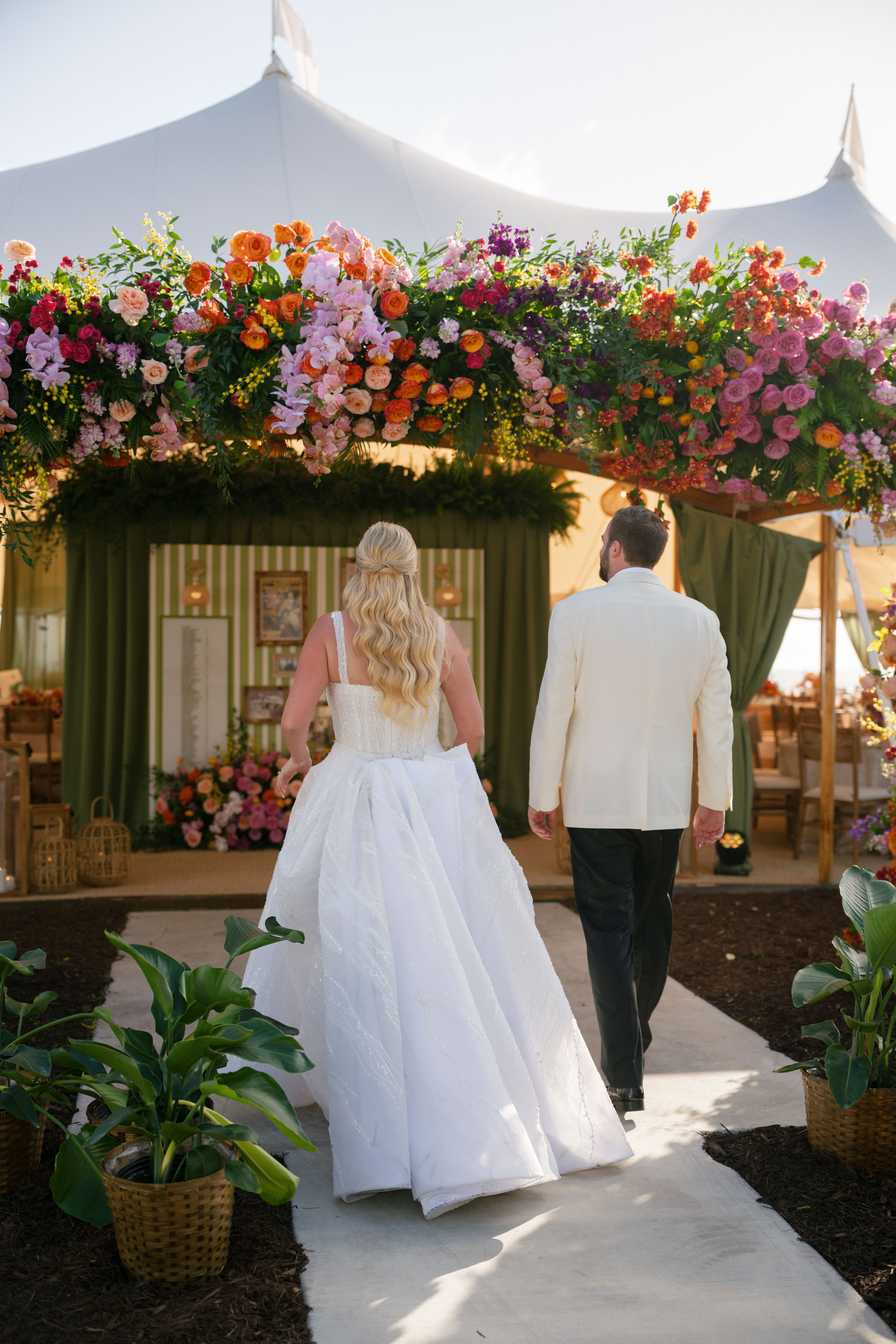 A bride and groom walking into their Florida tented reception with a floral arch and green seating chart.