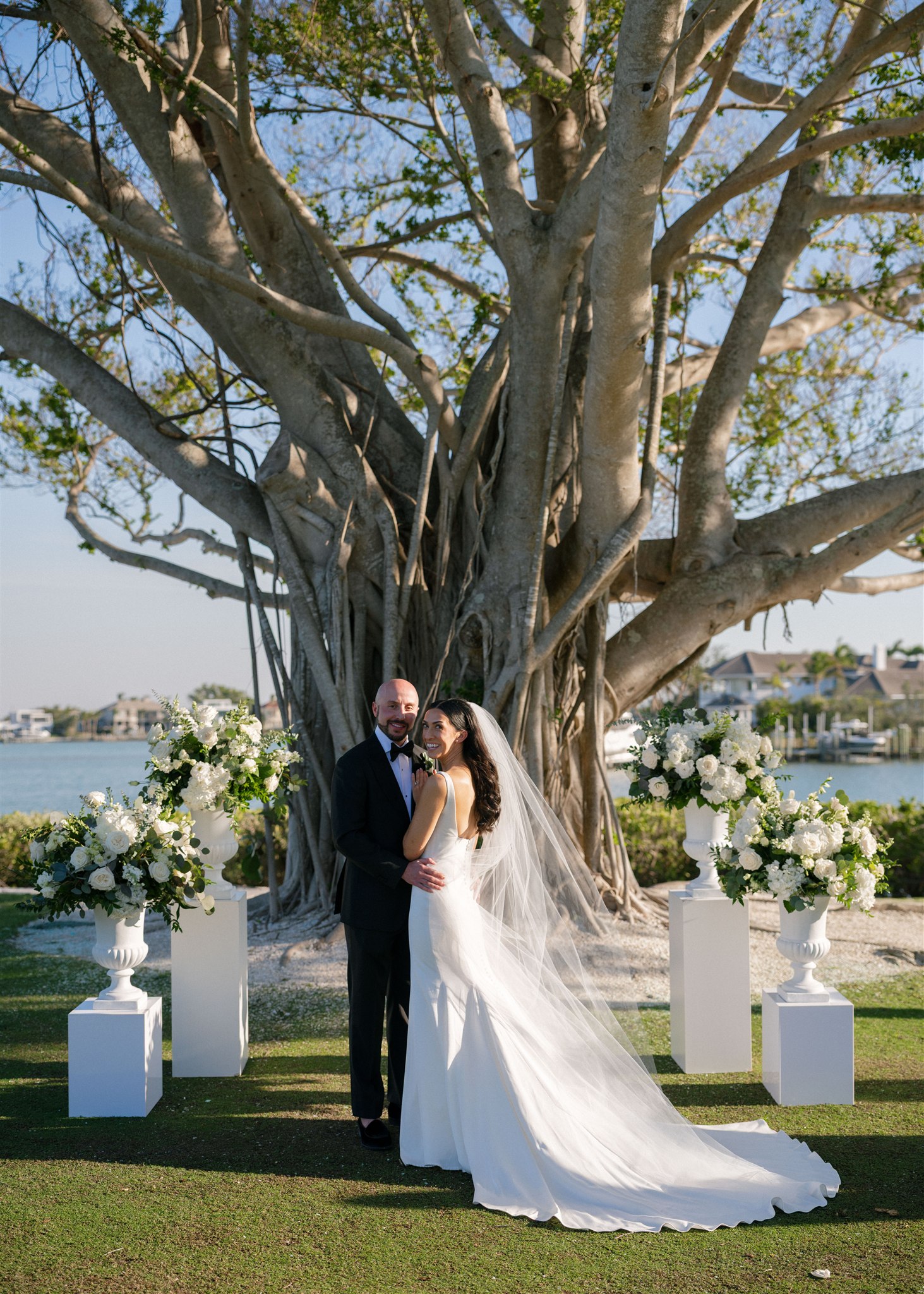 A bride and groom pose for portraits in front of a large tree at the ceremony altar.