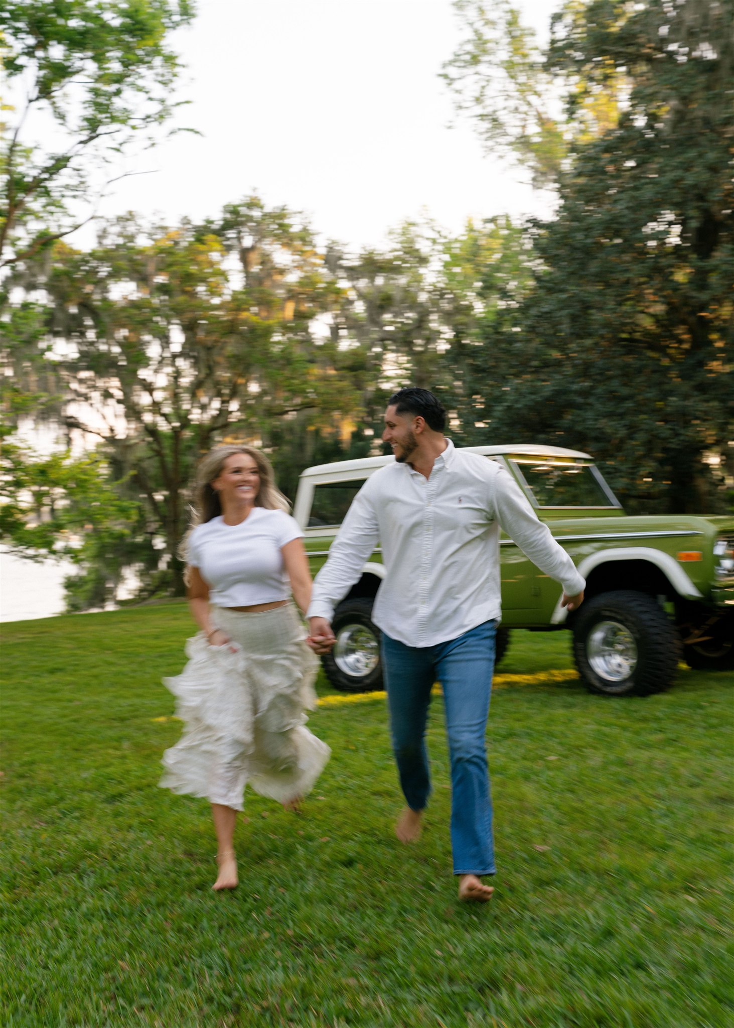 A couple running towards the camera with a vintage green Bronco behind them.
