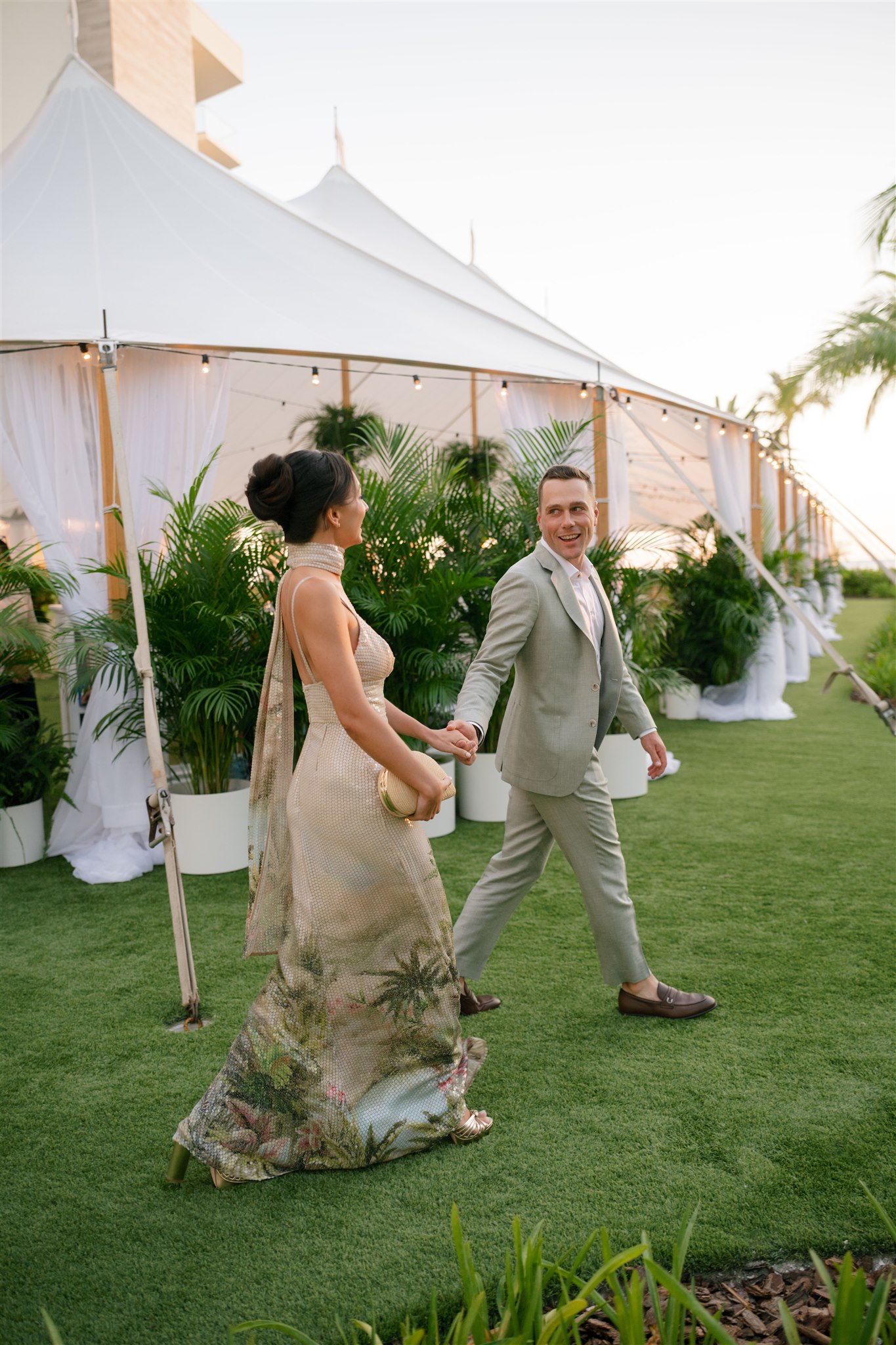 A couple strolling hand in hand in front of a tented wedding welcome party at the St Regis Lonboat Key Resort.