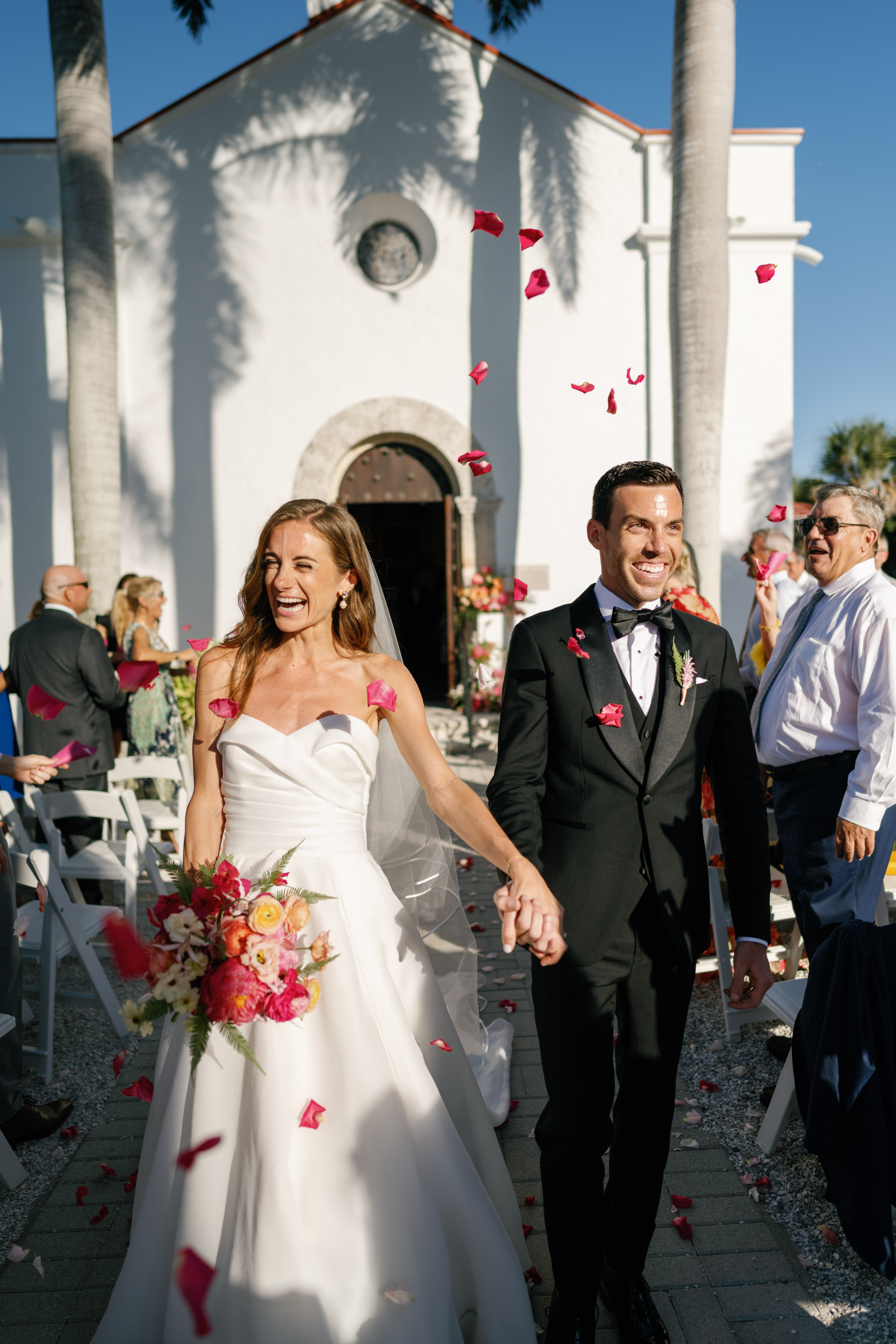A bride and groom leaving their traditional church wedding ceremony with petals flying in the air.