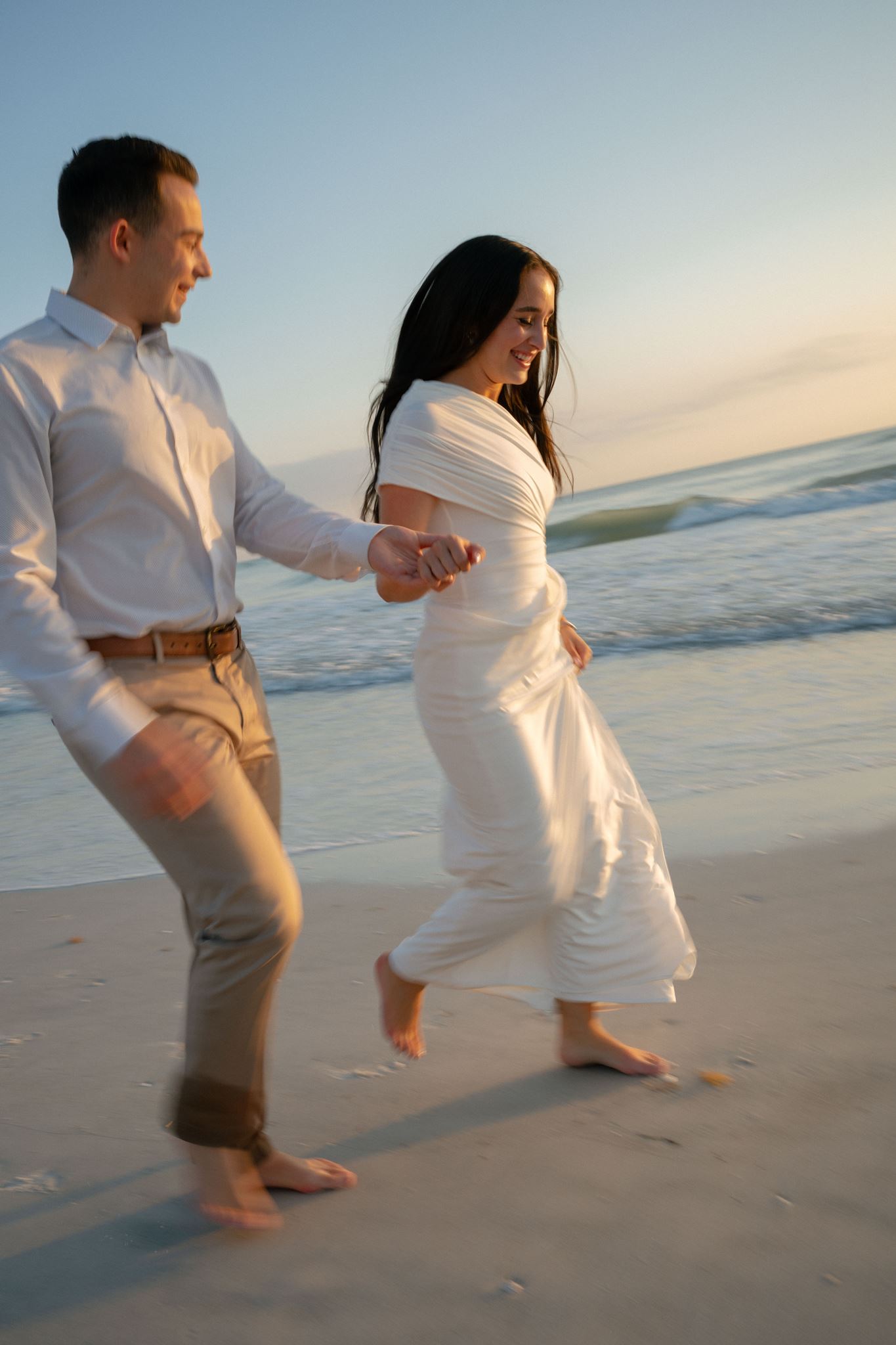 An engaged couple runs down the Florida beach at sunset, hand in hand.