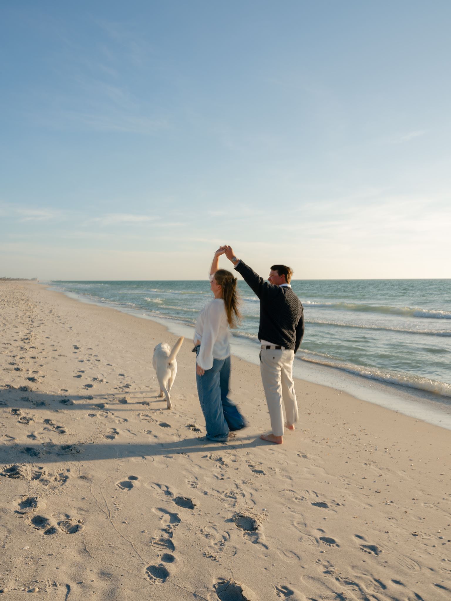 A couple dancing on the beach with their yellow lab at golden hour.