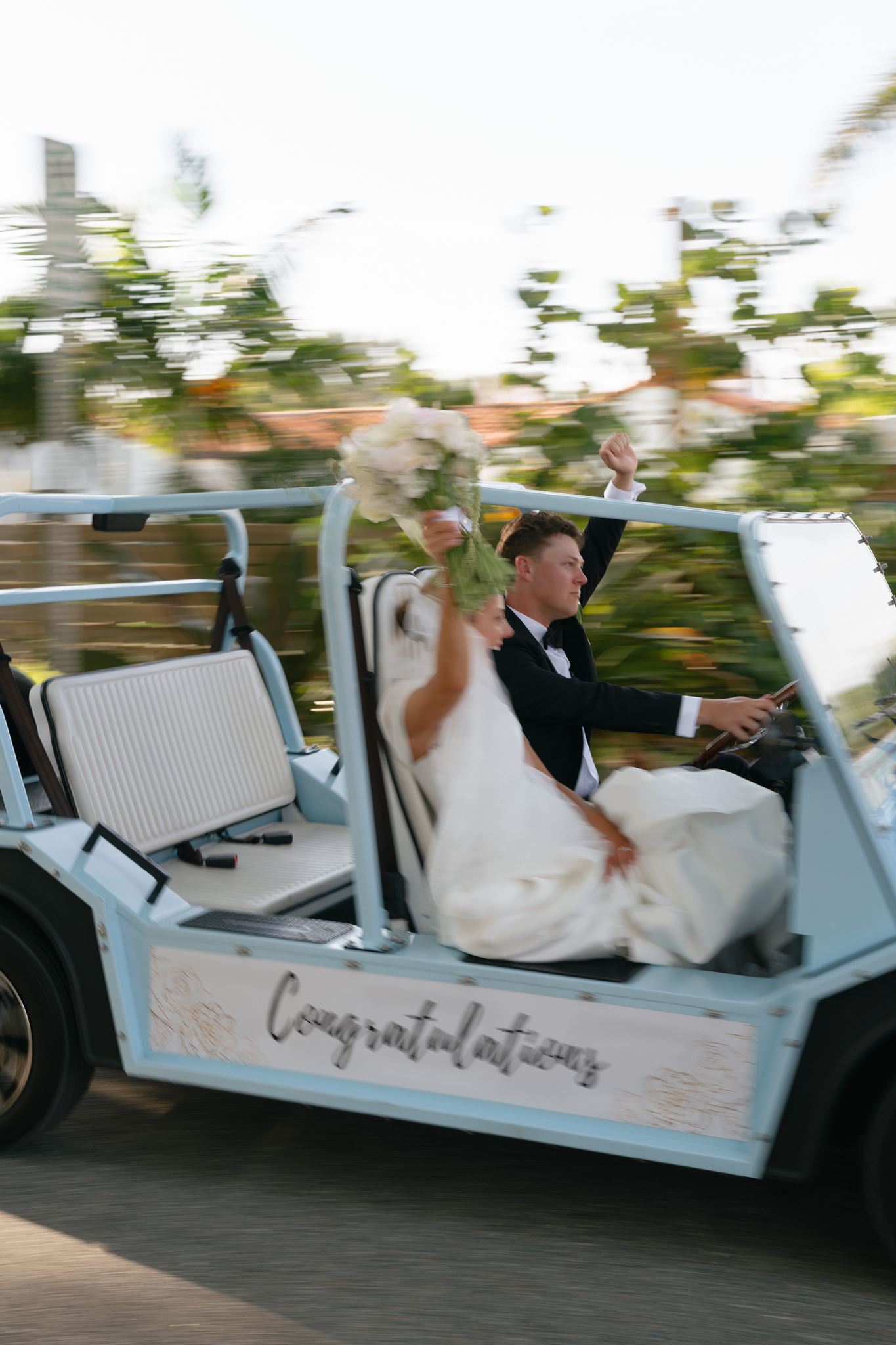 A bride and groom take off in a baby blue topless car after their wedding ceremony.